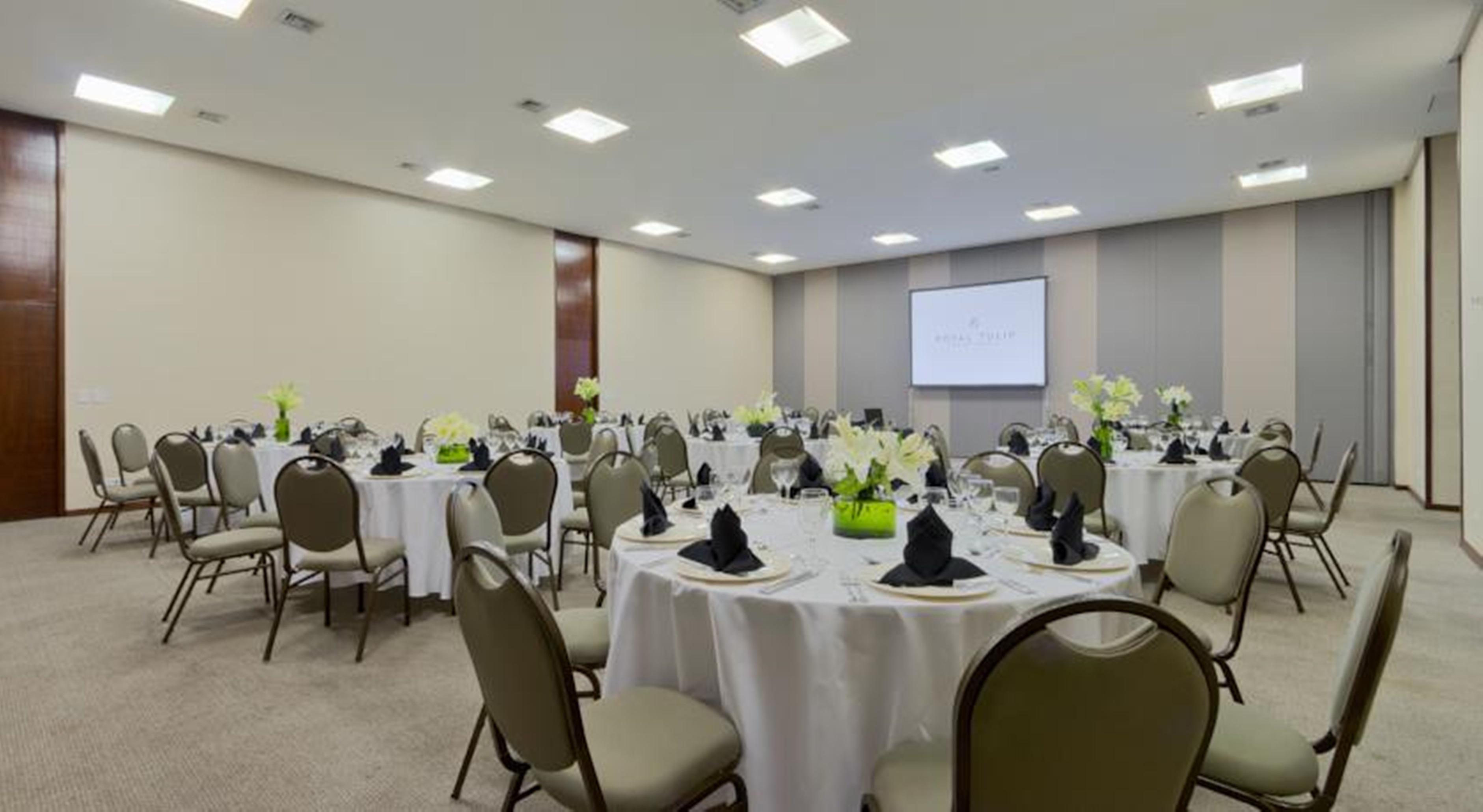 Royal Tulip Brasilia Alvorada Hotel Exterior photo The photo shows a banquet or conference room set up with multiple round tables covered in white tablecloths. Each table is arranged with black napkins and centerpieces featuring flowers, likely in shades of green and white. The room has beige walls a