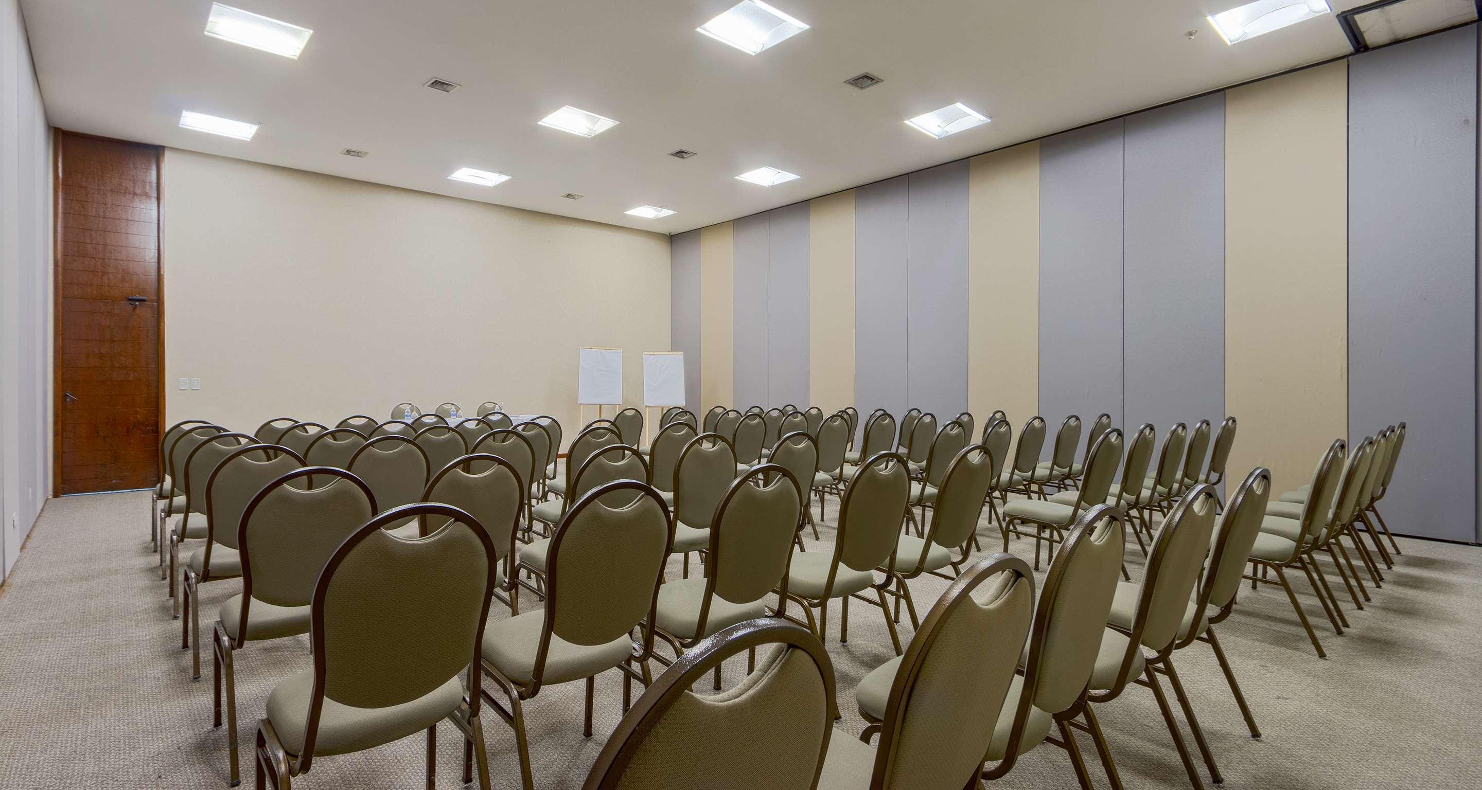 Royal Tulip Brasilia Alvorada Hotel Exterior photo The photo shows an empty conference room or meeting space. There are numerous rows of beige chairs arranged in a grid pattern, indicating the area is set up for an event. The walls are a light color with sections of gray soundproofing panels, and the