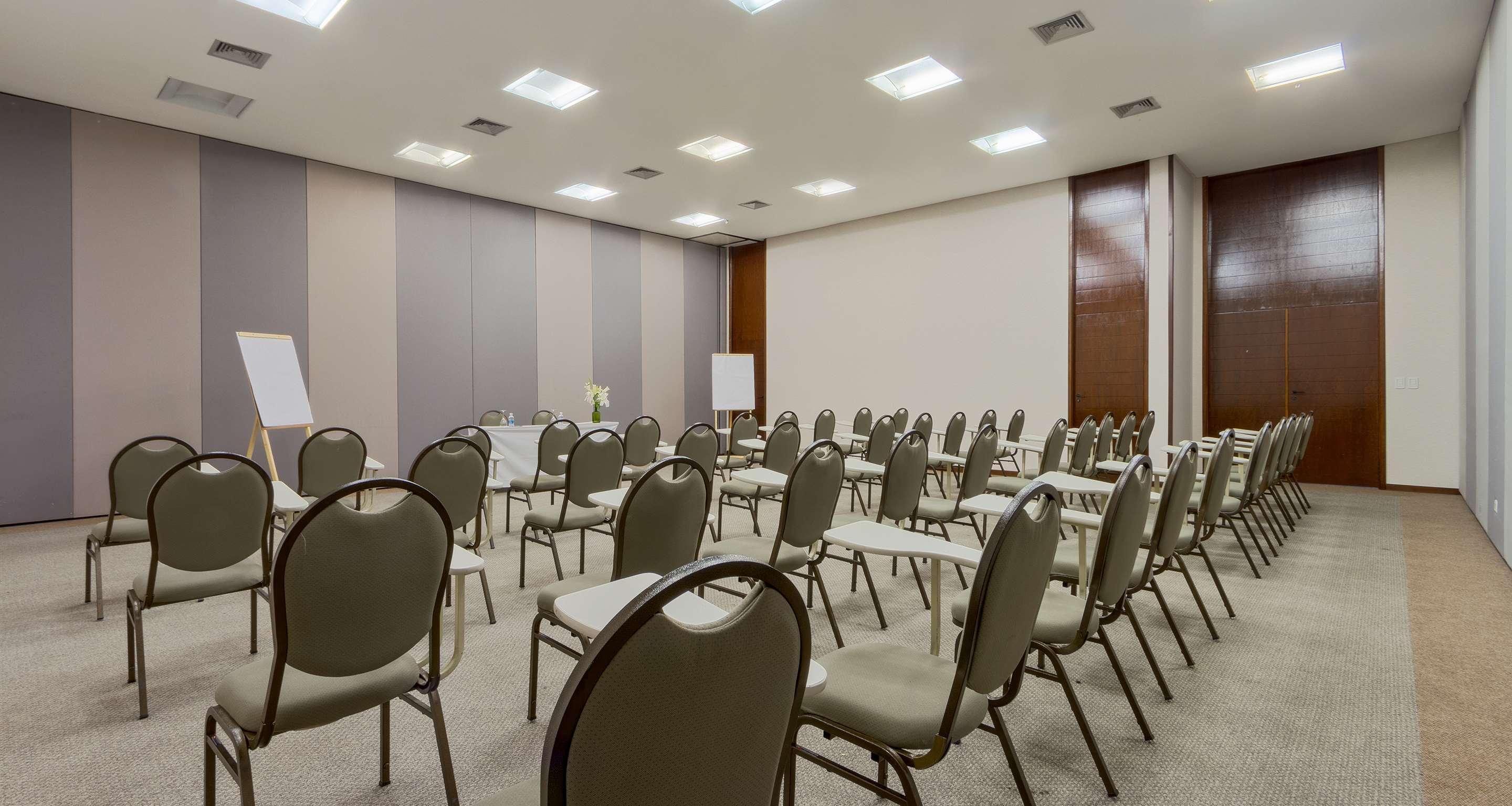 Royal Tulip Brasilia Alvorada Hotel Exterior photo The photo shows a conference or meeting room set up with multiple rows of chairs facing the front. The chairs are arranged neatly and have a light, neutral color. Along one side of the room, there is a table set up, likely for presenters or speakers,