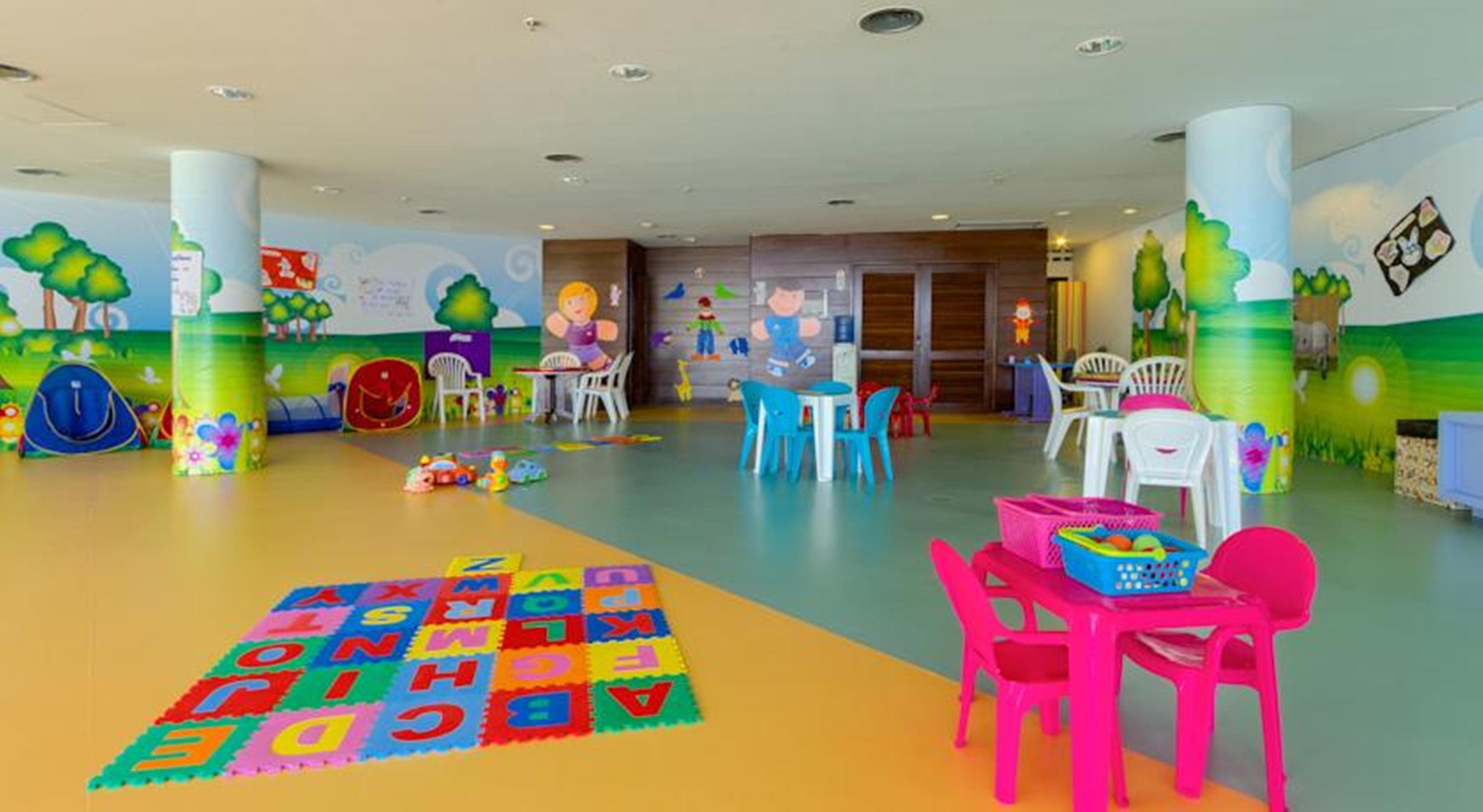 Royal Tulip Brasilia Alvorada Hotel Exterior photo The photo shows a colorful and spacious children's playroom. The floor is divided into sections with different colors, and there is a large play mat featuring letters and numbers. 

In the room, there are several small, lightweight tables and chairs 