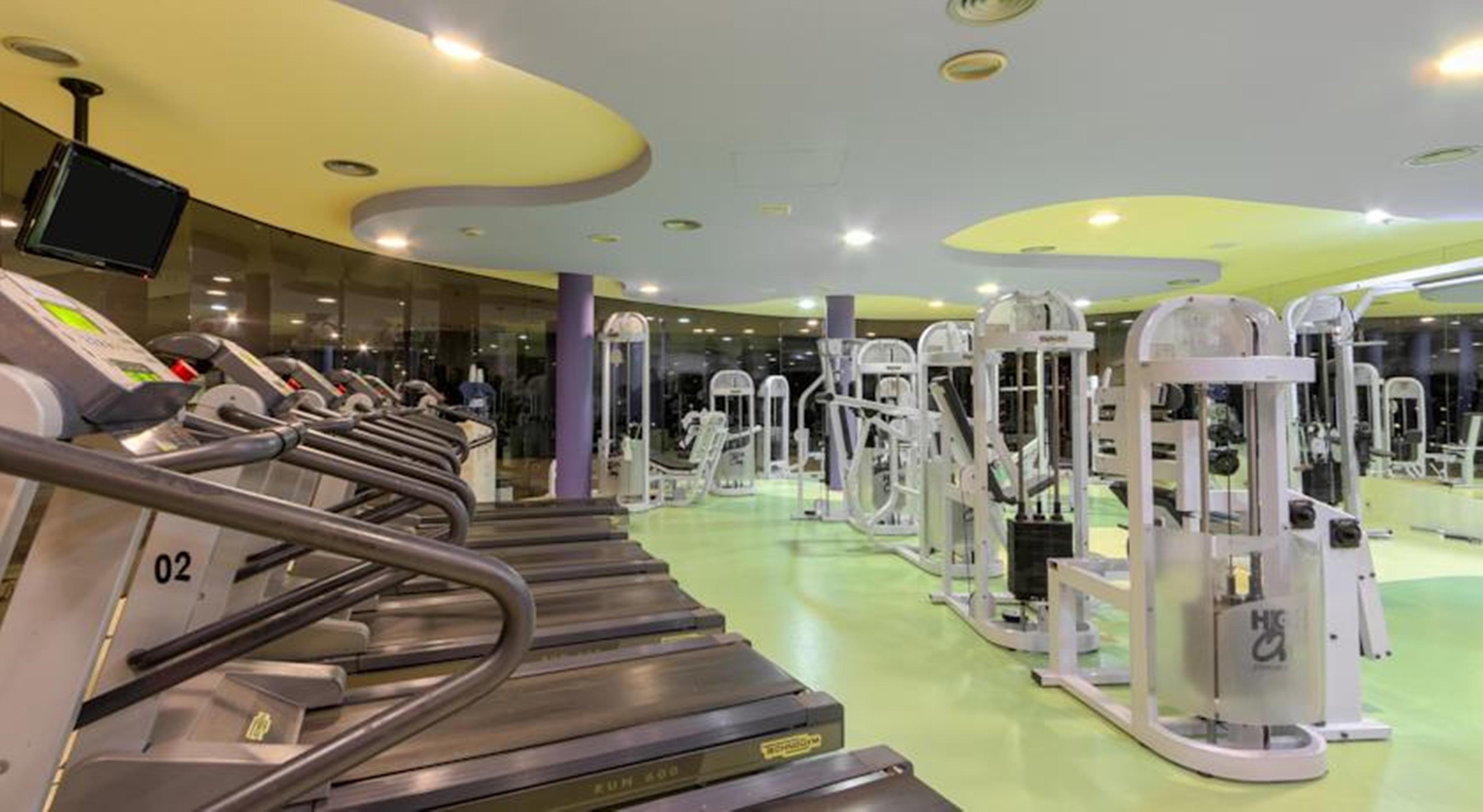 Royal Tulip Brasilia Alvorada Hotel Exterior photo The photo shows the interior of a gym or fitness center. It features several treadmill machines lined up in the foreground, with various weight training and exercise machines visible in the background. The gym has a bright and modern design, with col